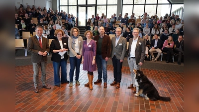 Freude über rund 250 Teilnehmende am Fachtag „Junge Menschen mit psychischen Belastungen in der beruflichen Orientierung“ in Höxter: (v.l.) Landrat Michael Stickeln, Moderatorin Susanne Stork, Caroline Rieger, Katrin Niemann (beide Kommunalen Koordinierungsstelle Übergang Schule-Beruf des Kreises Höxter), Dominic Gehle (Leiter der Abteilung Bildung und Integration des Kreises Höxter), Stefan Fellmann (Dezernent für Schulen, Ordnung, Soziales und Recht der Stadt Höxter) und Referent Dr. Dirk Dammann (Leiter der Klinik Albert-Schweizer-Therapeutikum in Holzminden) mit Hund Bagira. (Foto: Kreis Höxter)