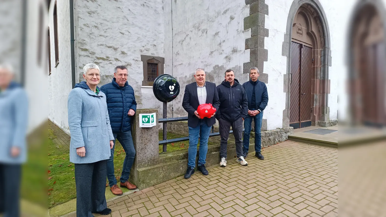 An der Kirche in Tietelsen und an der Halle in Rothe hängt jetzt jeweils ein Defibrillator. Möglich wurde dies durch viele Spenden. (v.l.) Brigitte Kutz (Volksbank Höxter), Rüdiger Hölscher (Westfalen Weser), Jörg Hiltafsky (Sparkasse Paderborn-Detmold-Höxter), Tobias Antenbrink (Antenbrink Bau) und Bernd Sievers (Sieversbau) nahmen die grünen Lebensretter in Augenschein.  (Foto: M. Puls)