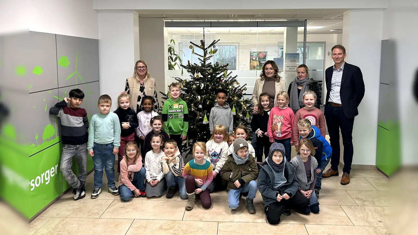 Die Kinder der 1A mit ihrer Lehrerin Frau Rüther-Lommel sowie Carmen Watermeyer-Fels, Irma Sabotic und Michael Starp (v.l.) von der BeSte vor dem bunt geschmückten Weihnachtsbaum. (Foto: BeSte Stadtwerke GmbH)